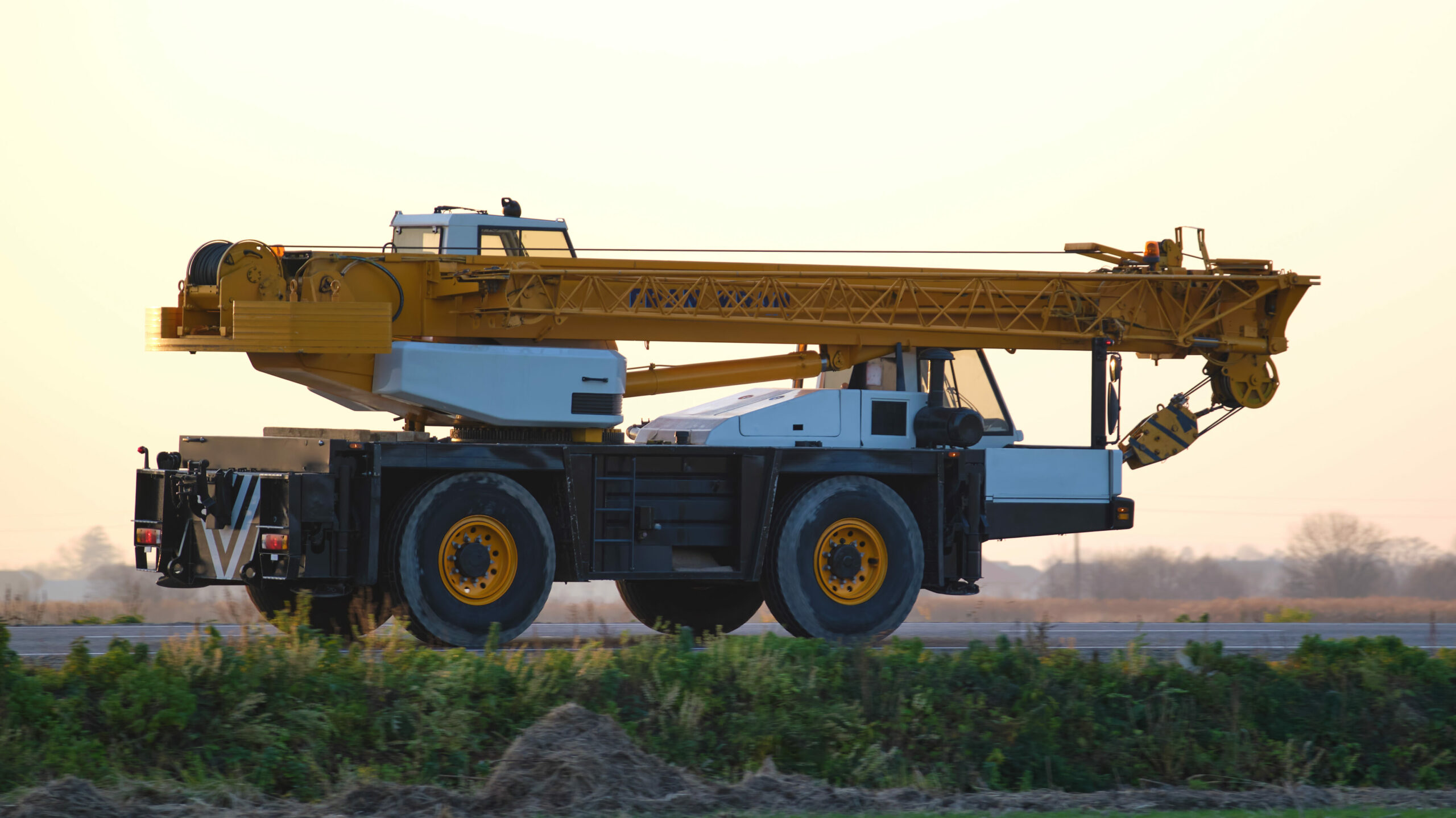 Grue mobile de levage lourde circulant sur une route de campagne.