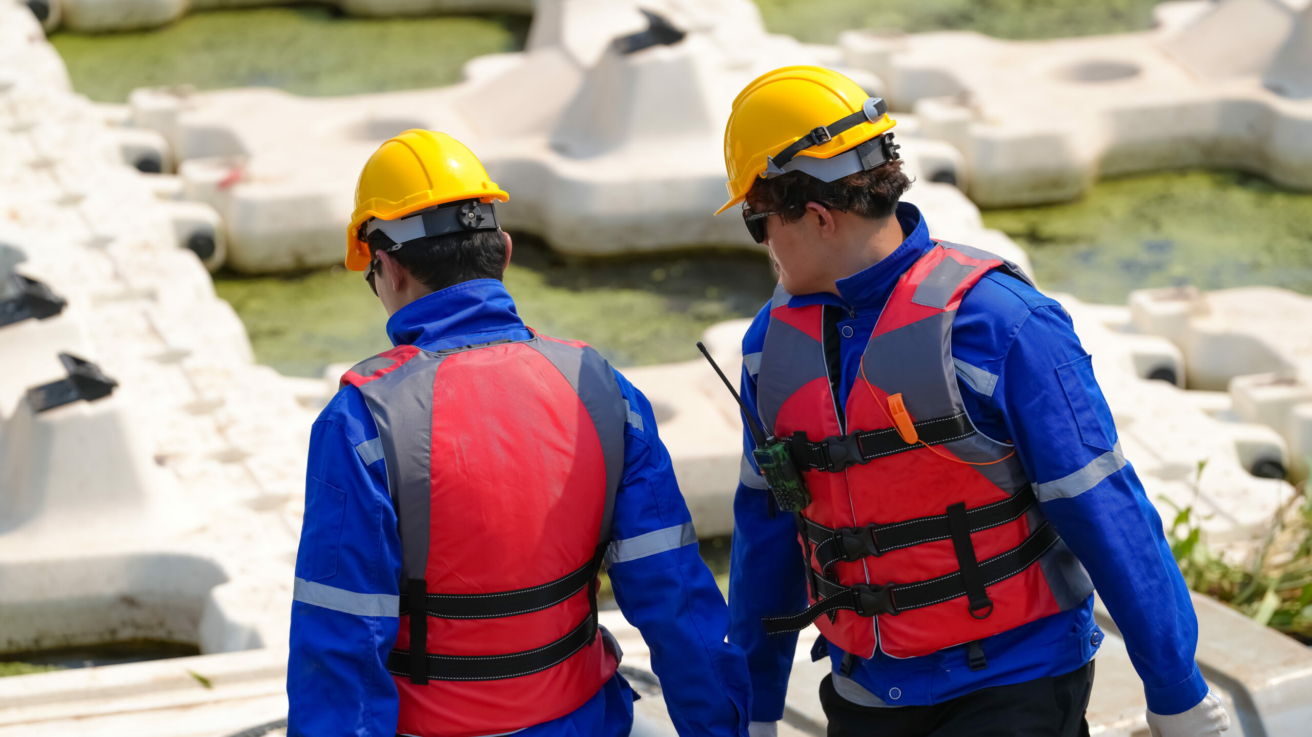 Deux professionnels portent des gilets d’aide à la flottabilité près d’une zone de travaux au bord de l’eau.