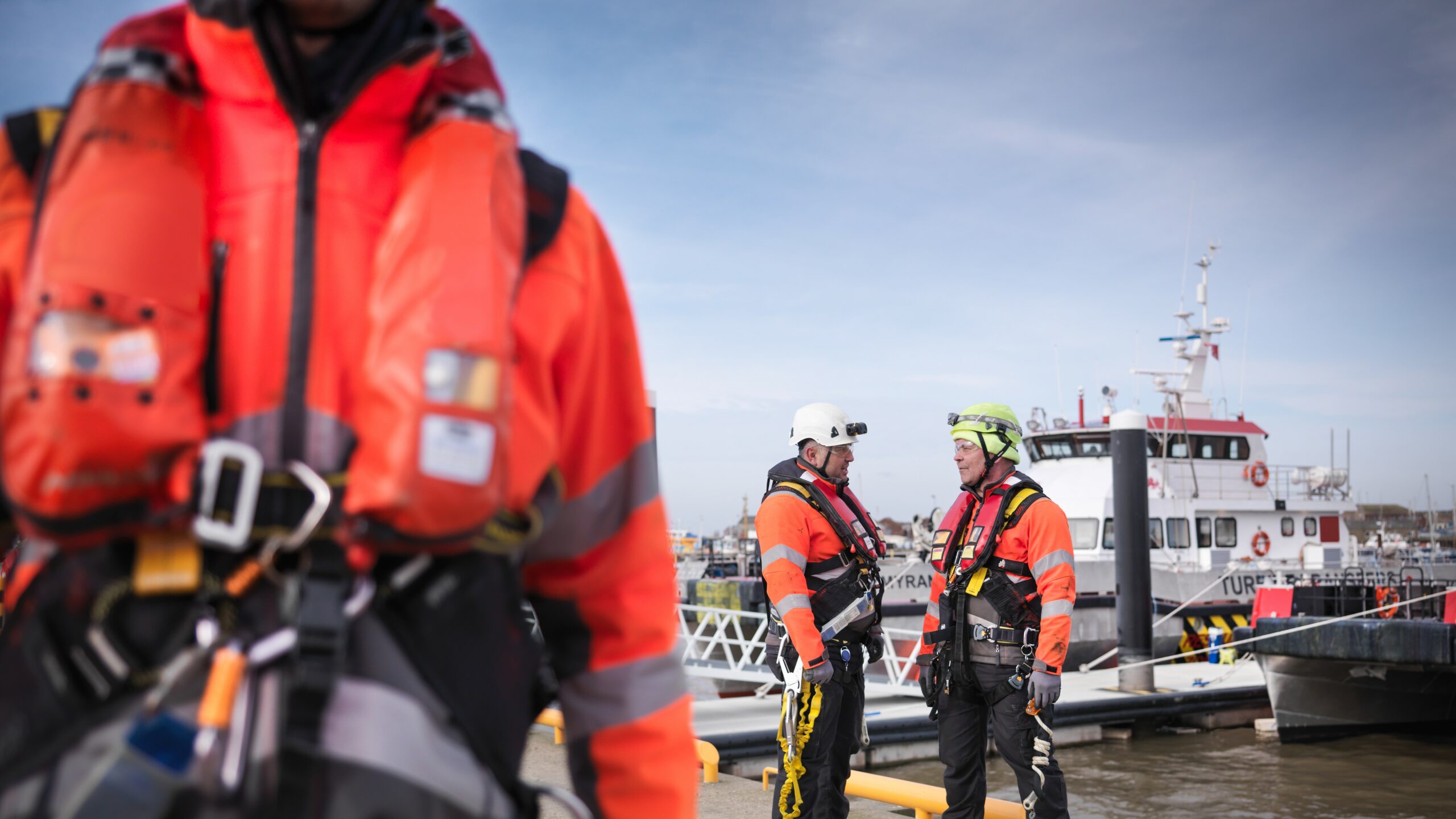 Travailleurs équipés de gilets de sauvetage professionnels sur un quai à proximité d’un bateau.