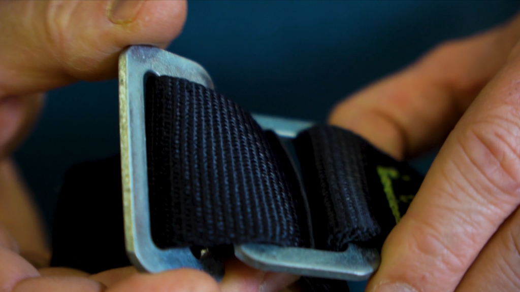 Gros plan sur une boucle métallique de réglage et une sangle noire d'un harnais antichute.